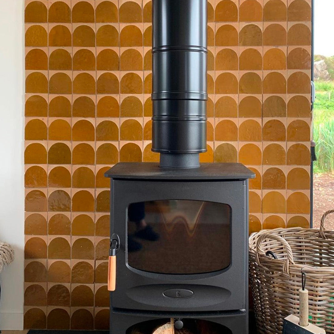Black wood stove against a patterned orange wall with a basket of logs.