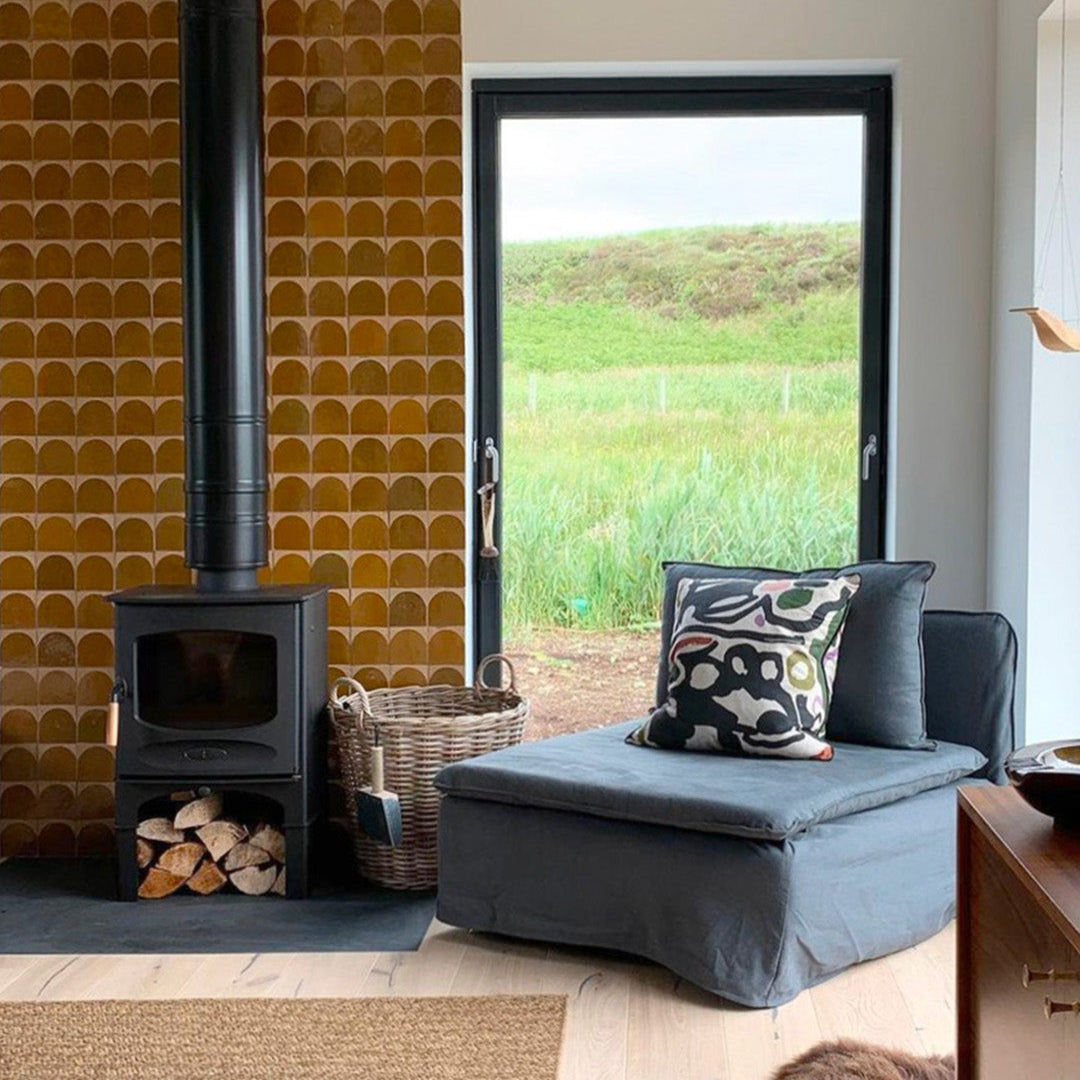 Living room with a wood stove, cushioned bench, and window view of greenery.