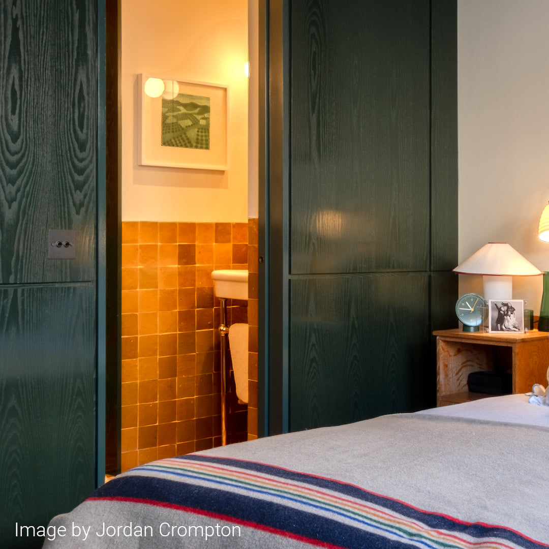 Bedroom with green sliding door, tiled wall, and nightstand with lamp and clock.