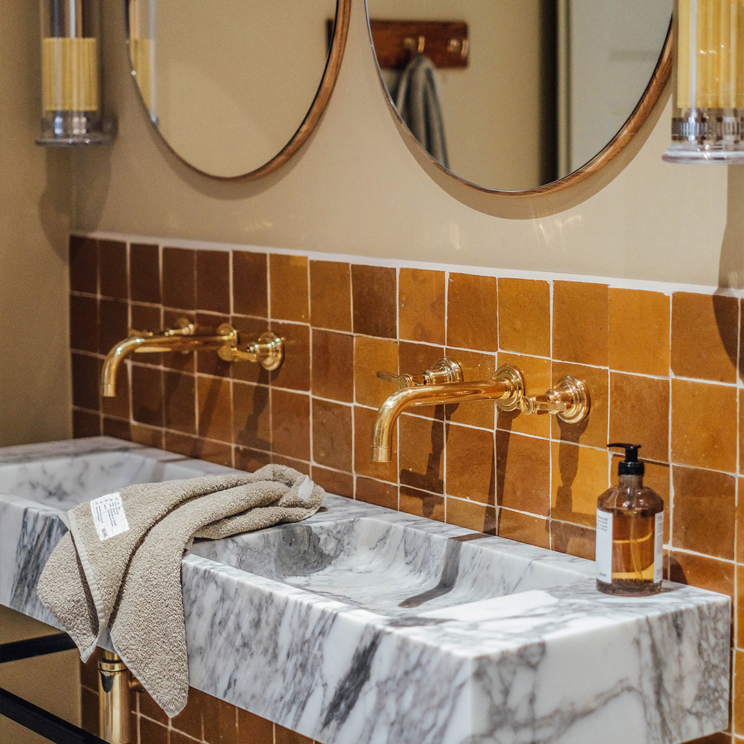 Bathroom sink with marble countertop, gold fixtures, and orange tiles.