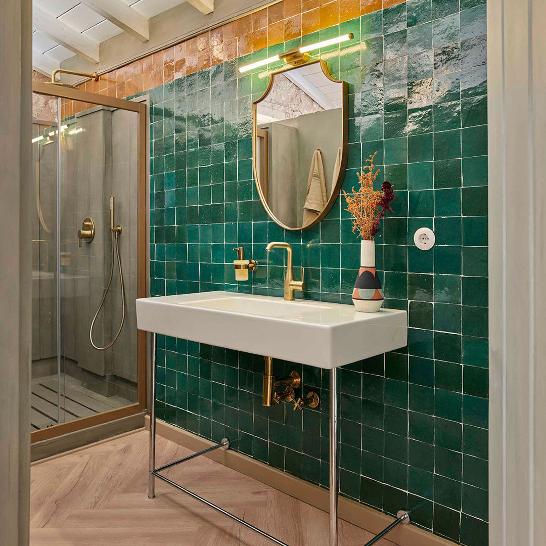 Bathroom with green tiled walls, white sink, and gold fixtures.
