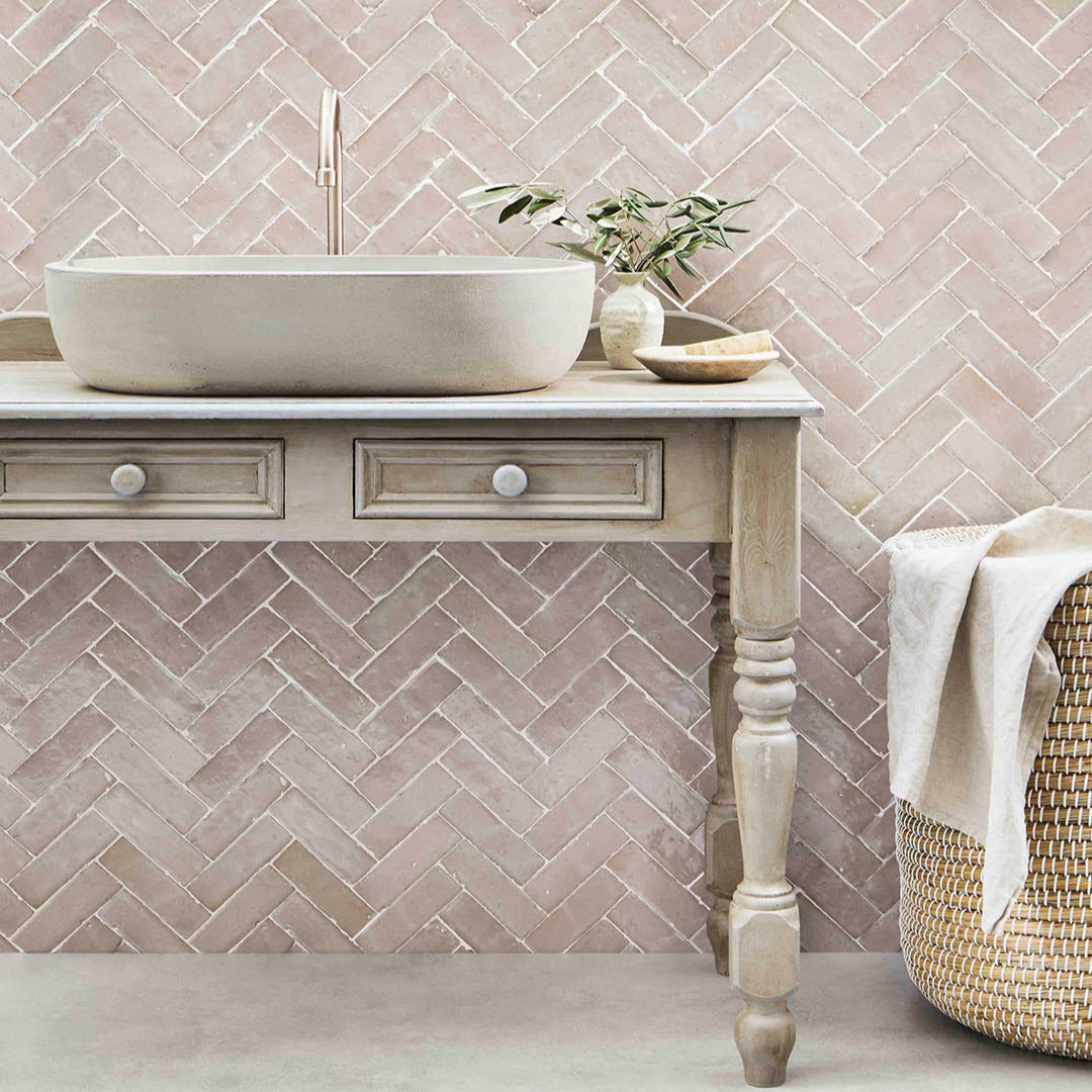 Bathroom with pink herringbone tile pattern on the wall, white sink, and wooden cabinet.