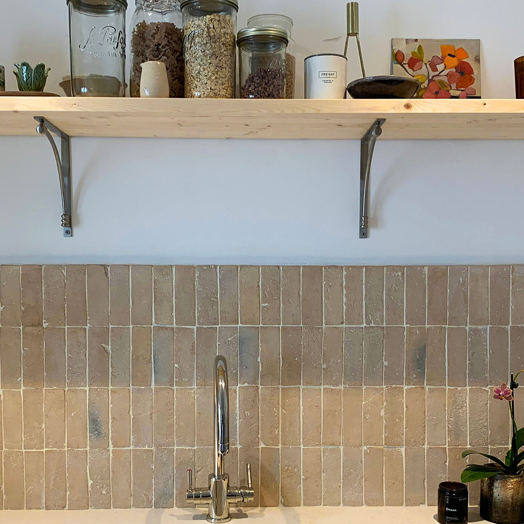 Vertical beige and brown ceramic backsplash tiles behind sink, paired with modern faucet, wooden shelf, and decorative bathroom accents.