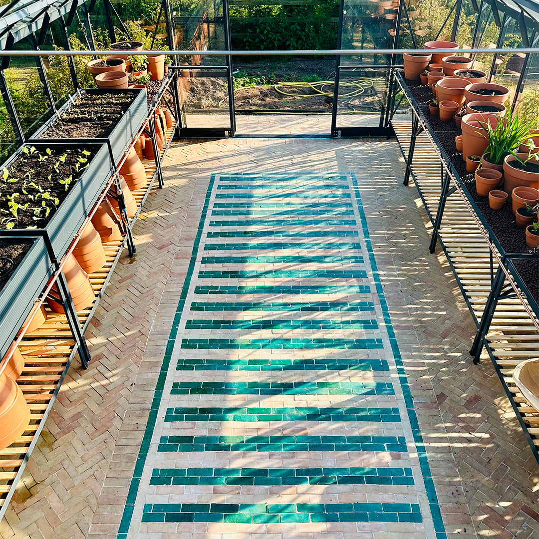 Striped green and beige bathroom mosaic tile flooring inside greenhouse, bordered with green tiles, blending decor and functionality.