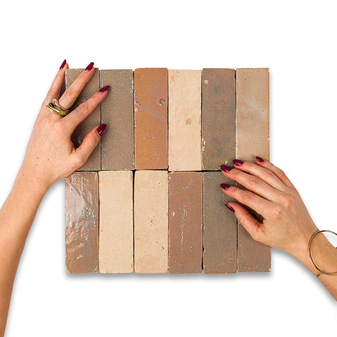 Beige, brown, and gray bathroom tiles in grid arrangement, framed by hands with maroon nails and gold ring.