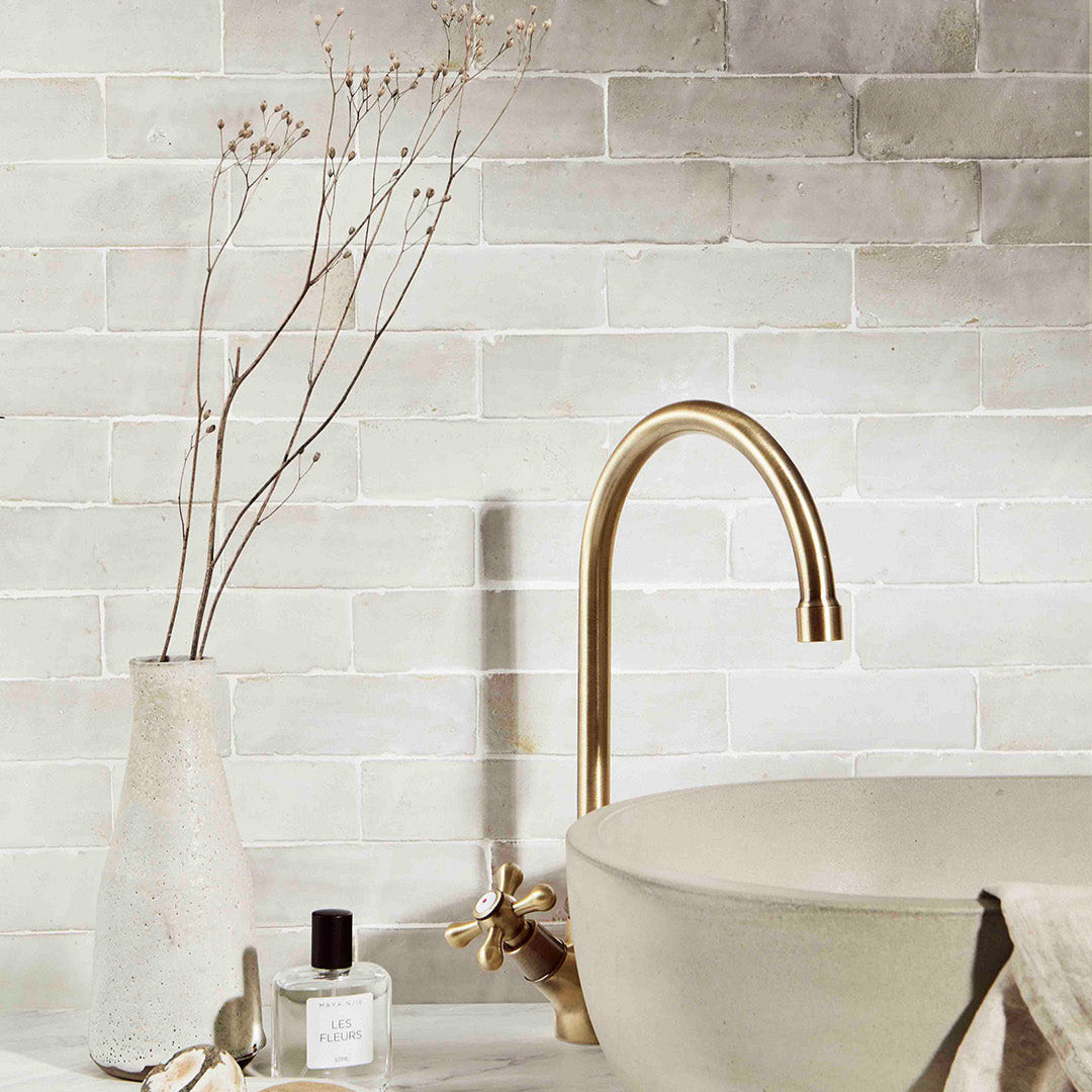 Bathroom setting with a gold faucet, sink, and decorative elements against a tiled wall.