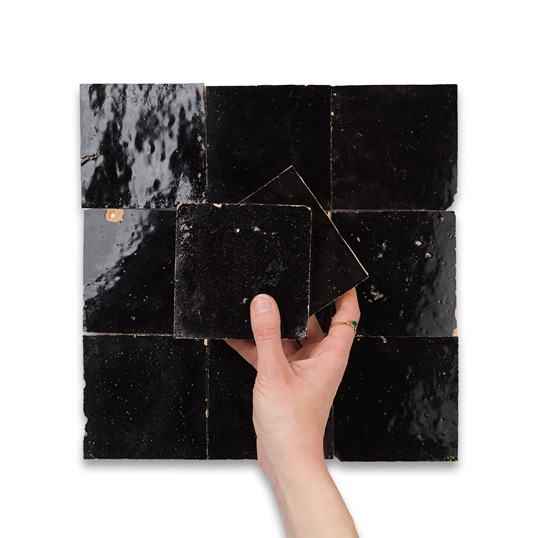 Hand holding a black square tile against a patterned black and gray tile background