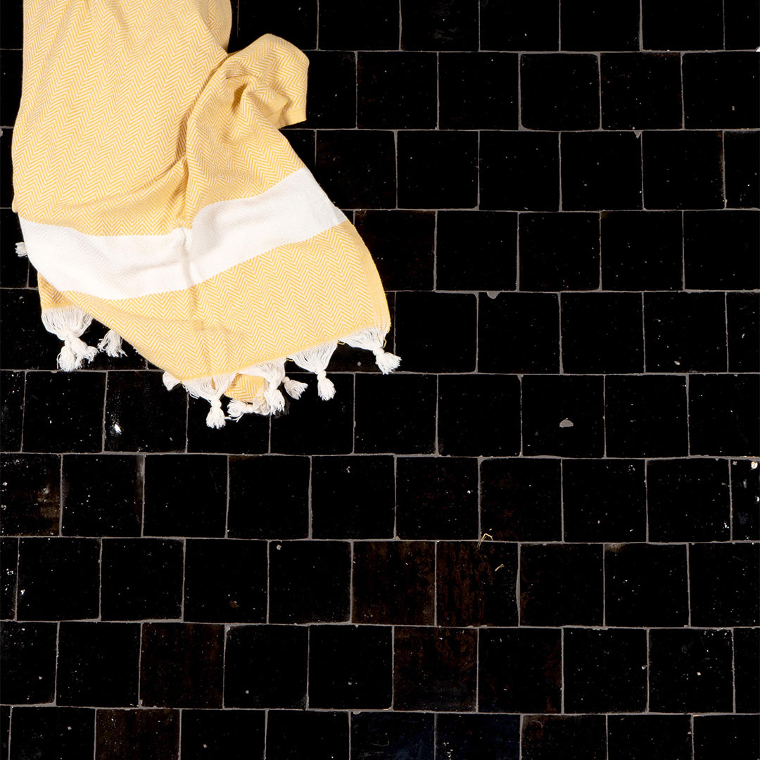 Yellow towel with white trim on a black tiled floor