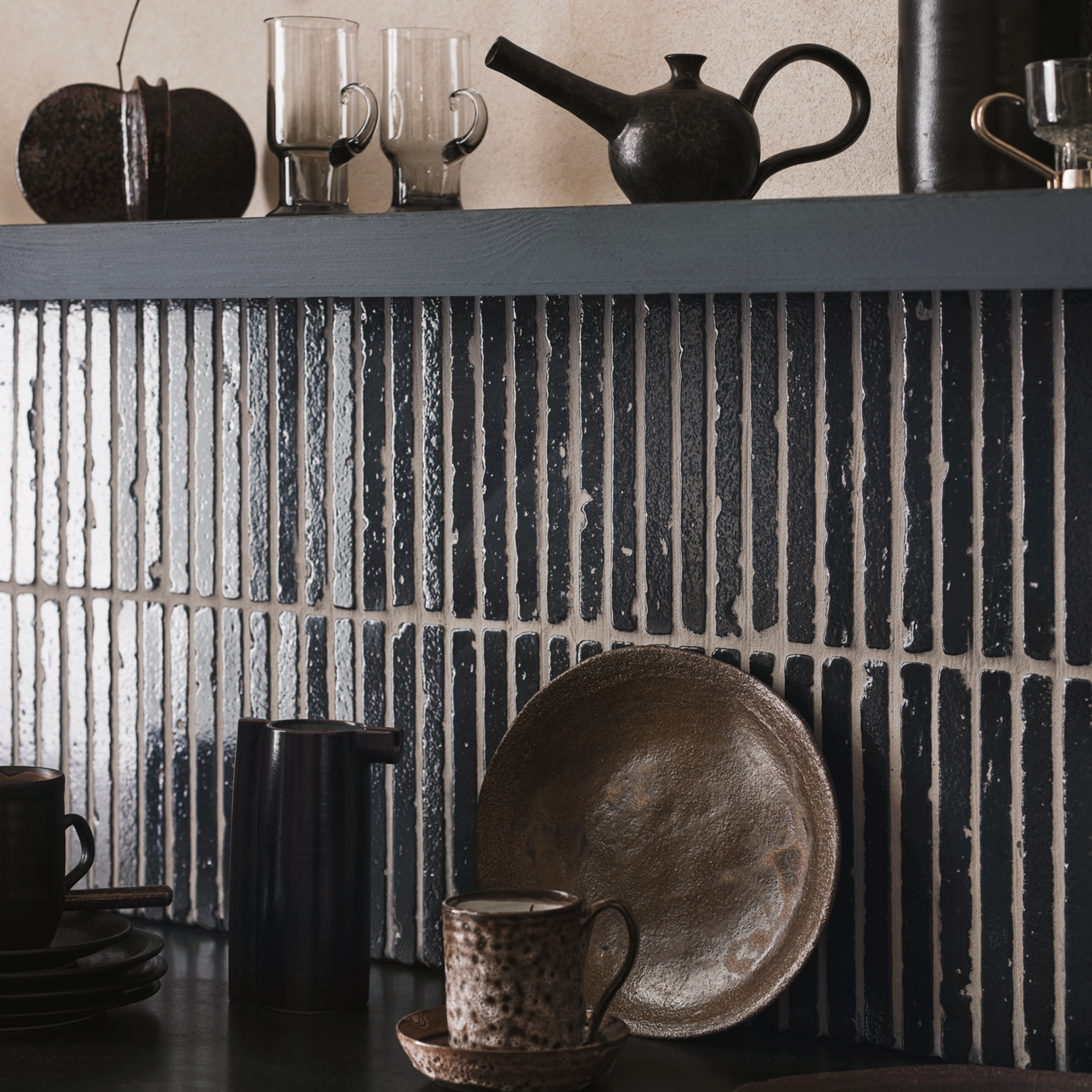 Dining area with black and brown ceramic plates and cups on a dark surface against a textured wall.