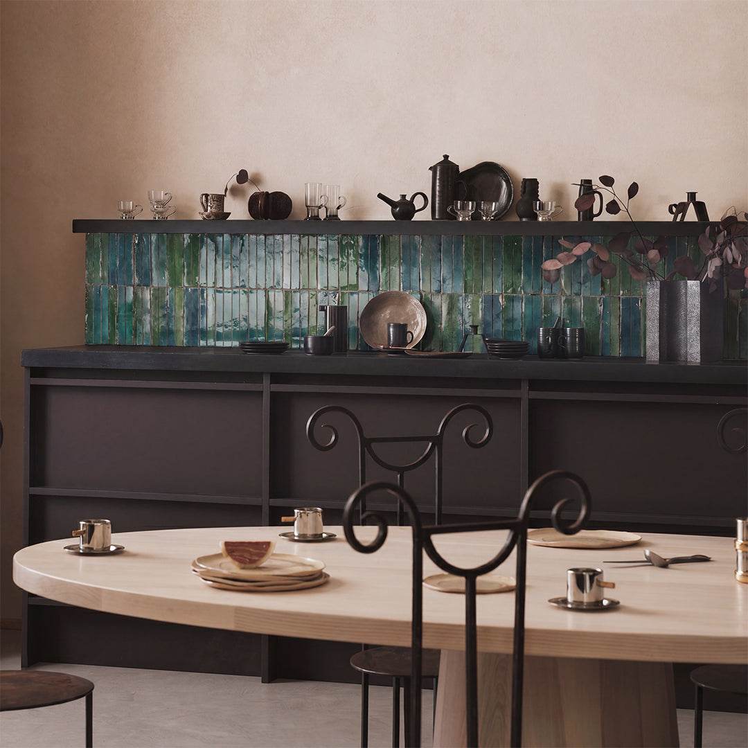 Dining area with a table and chairs in front of a dark wall with decorative elements.