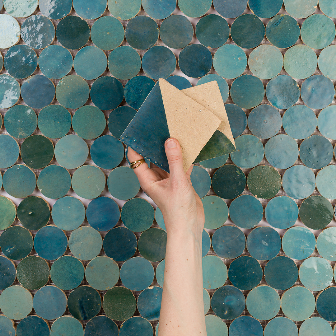 Hand holding two small tiles against a background of blue mosaic tiles
