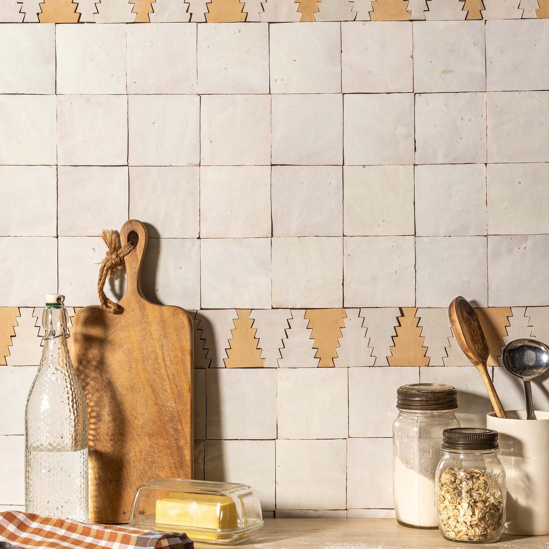 Kitchen counter with tiles featuring a geometric pattern, wooden cutting board, and various kitchen items.
