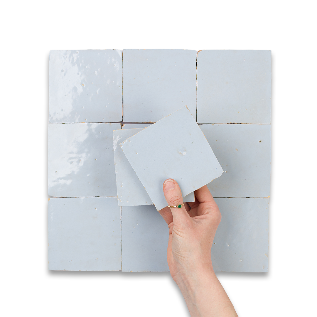 Hand holding a square tile against a tiled wall
