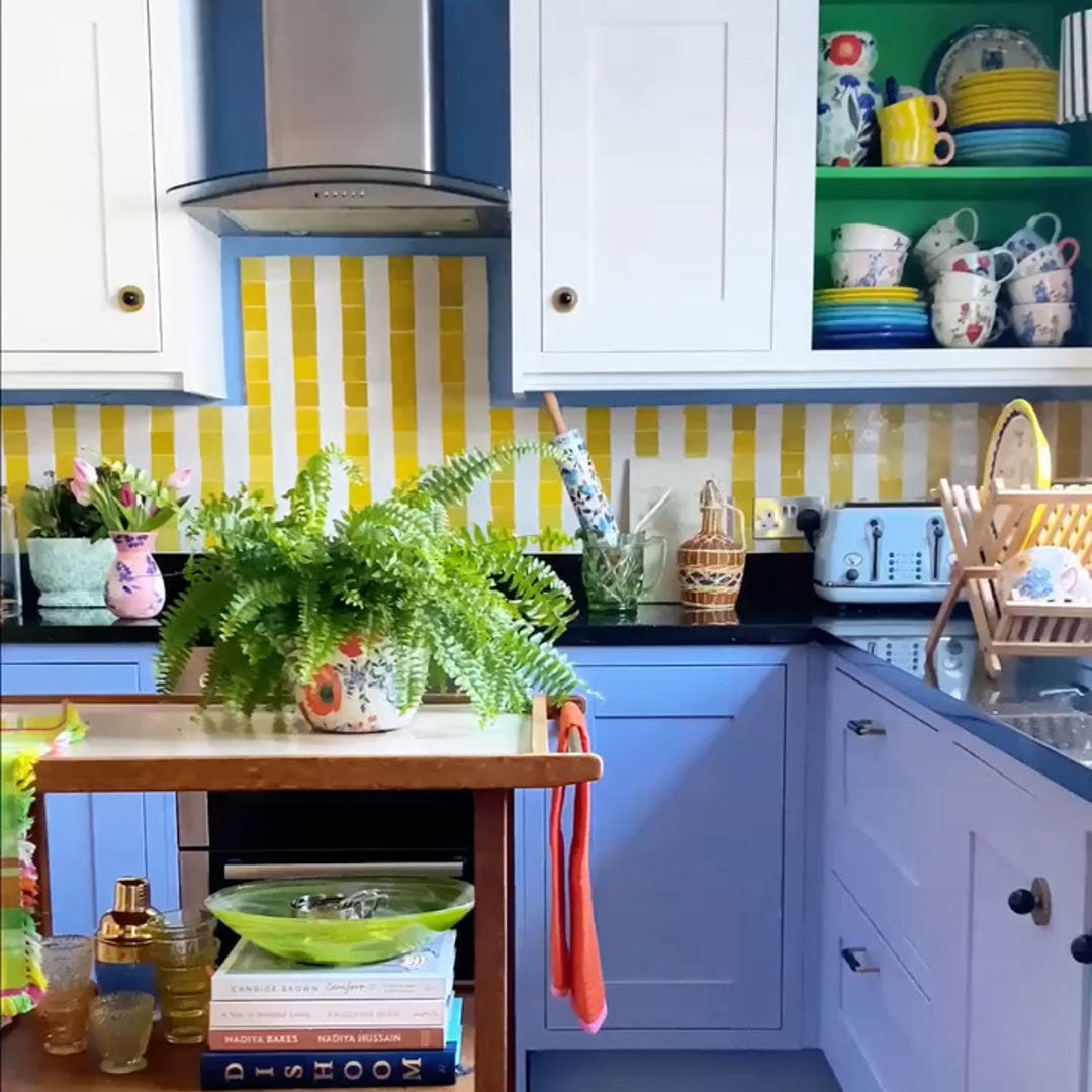 Colorful kitchen with blue cabinets, yellow striped backsplash, and various decor items.