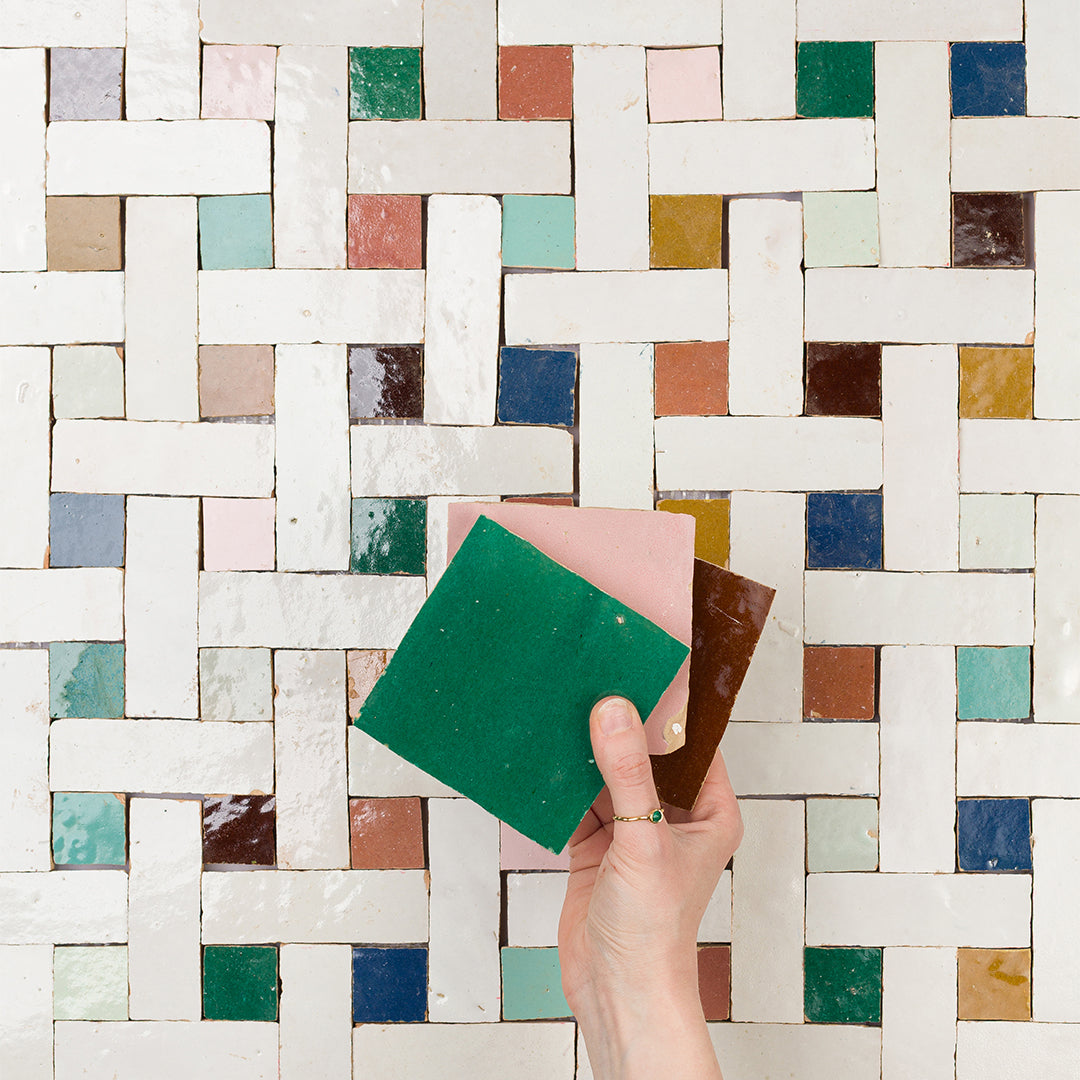 Hand holding a green sponge in front of a mosaic tile wall.