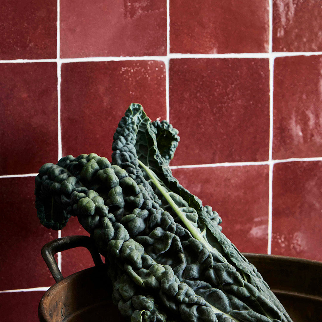 Bunch of green kale on a wooden surface with a red tiled wall background