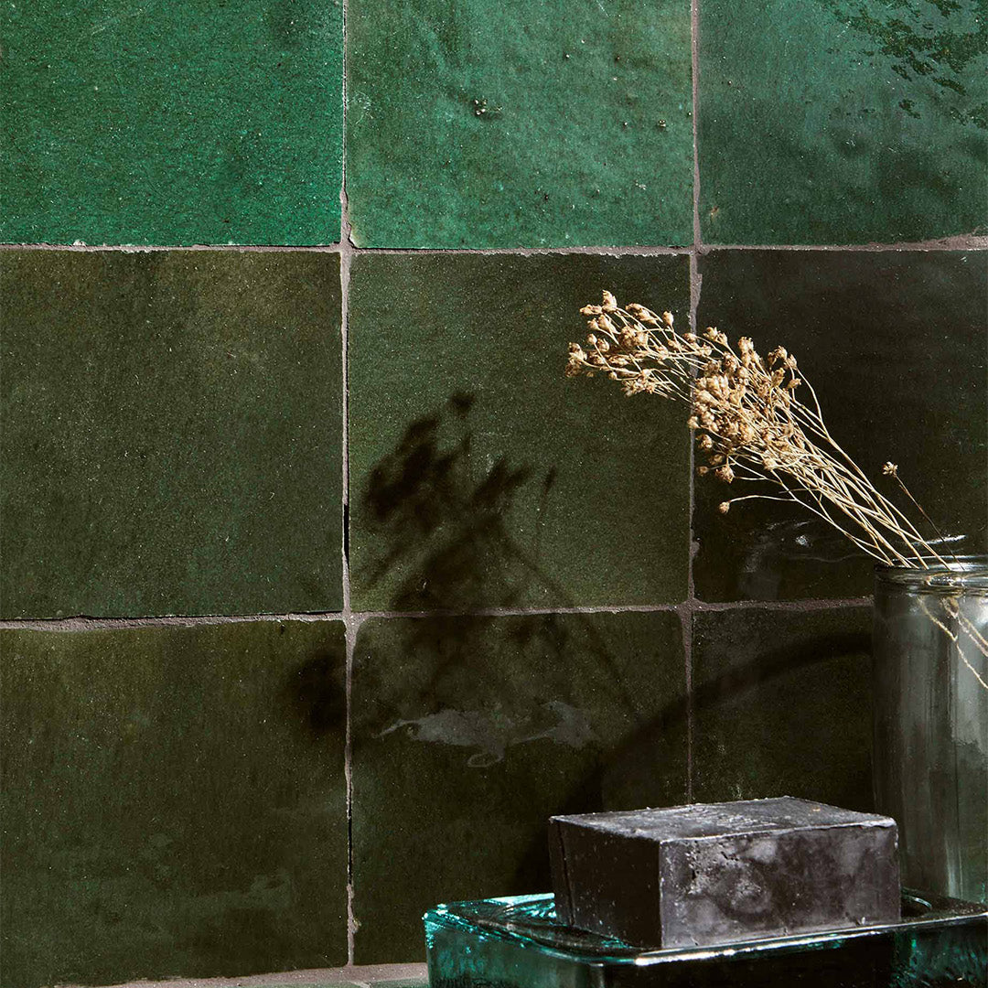 Green tiles with a vase and dried plants against a dark background