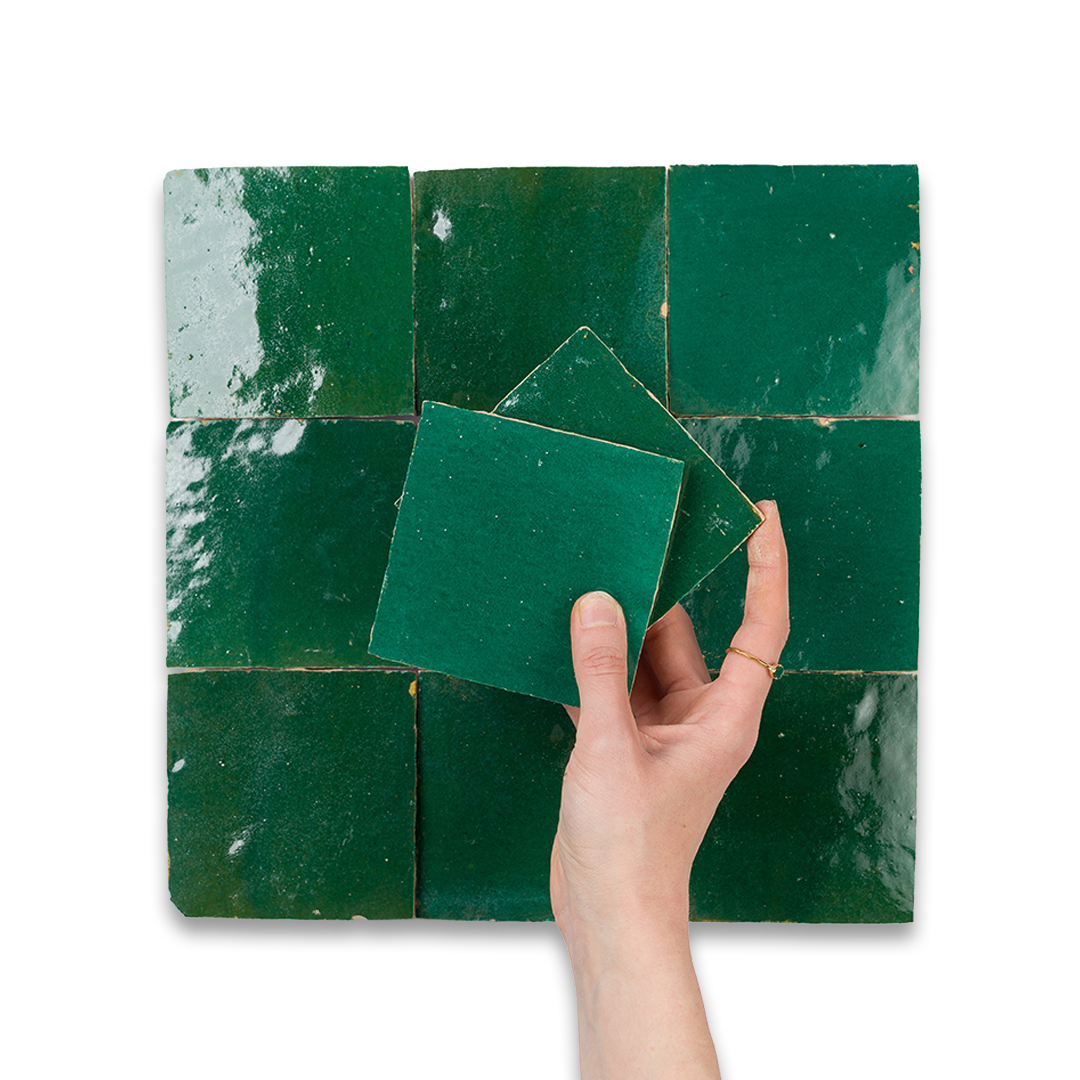 Hand holding green tiles against a tiled wall background