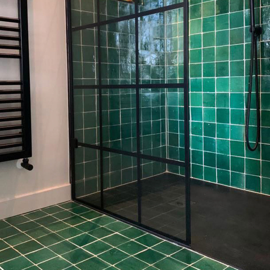 Green tiled shower with a black framed glass door