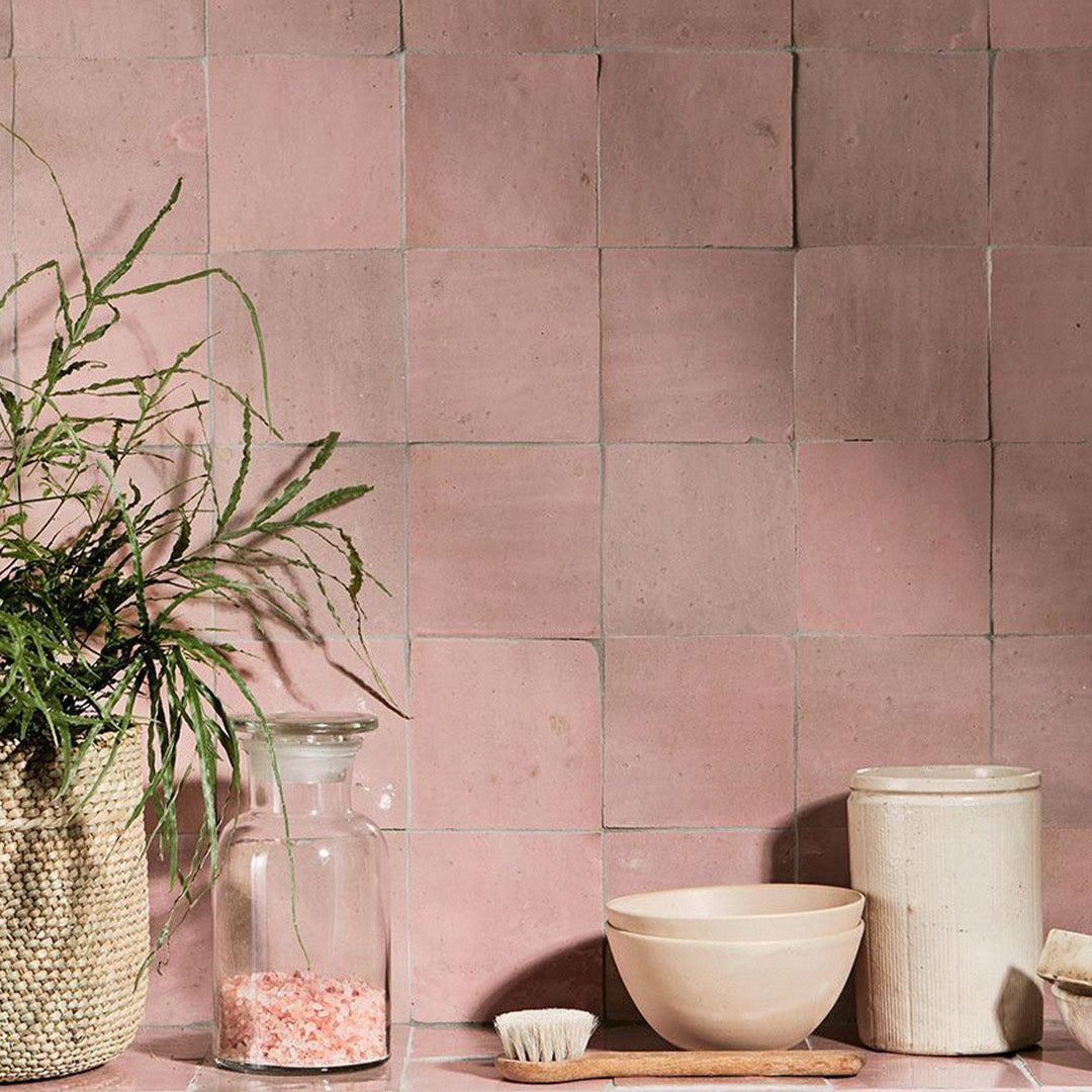 Pink tiled wall with decorative items including a plant, jar, bowl, and brush.