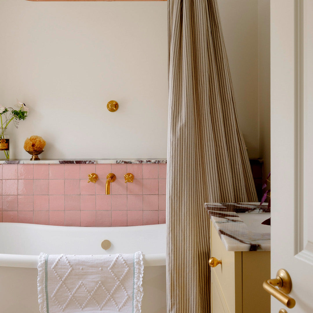 Bathroom with pink tiled wall, gold fixtures, and striped shower curtain.