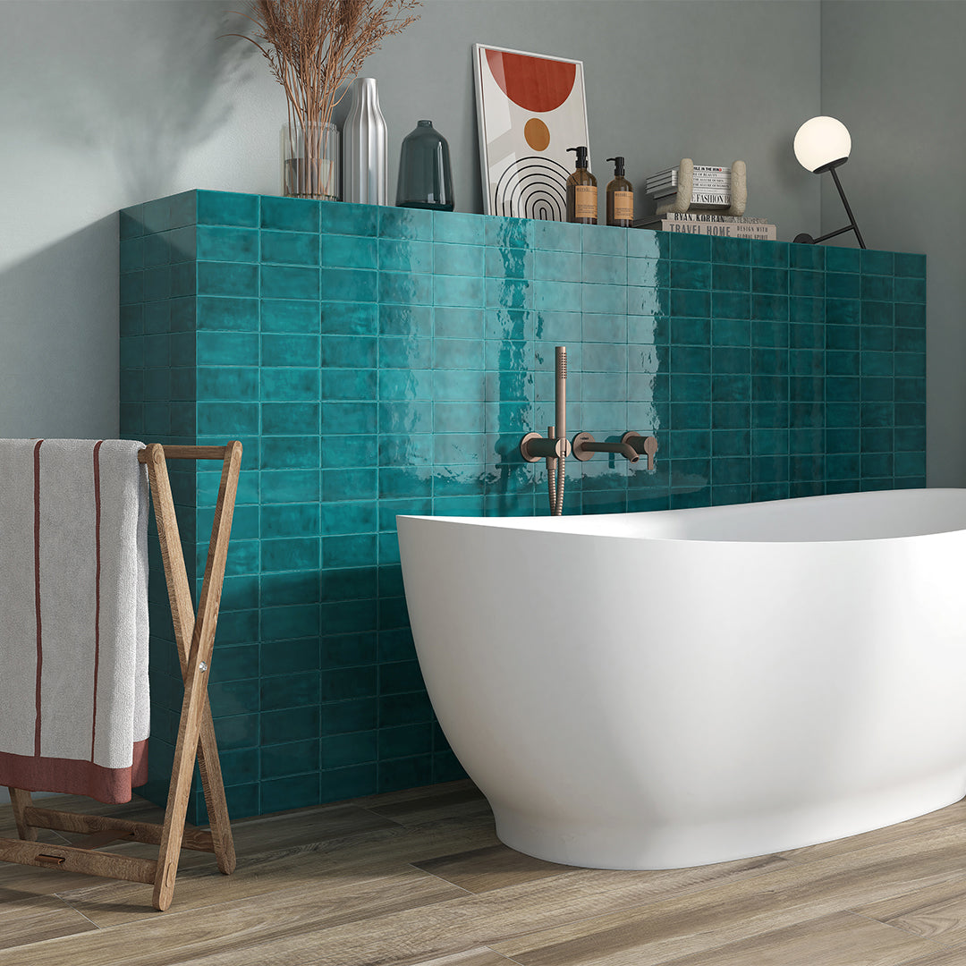 Modern bathroom with teal tiled wall, freestanding white bathtub, and wooden towel rack.