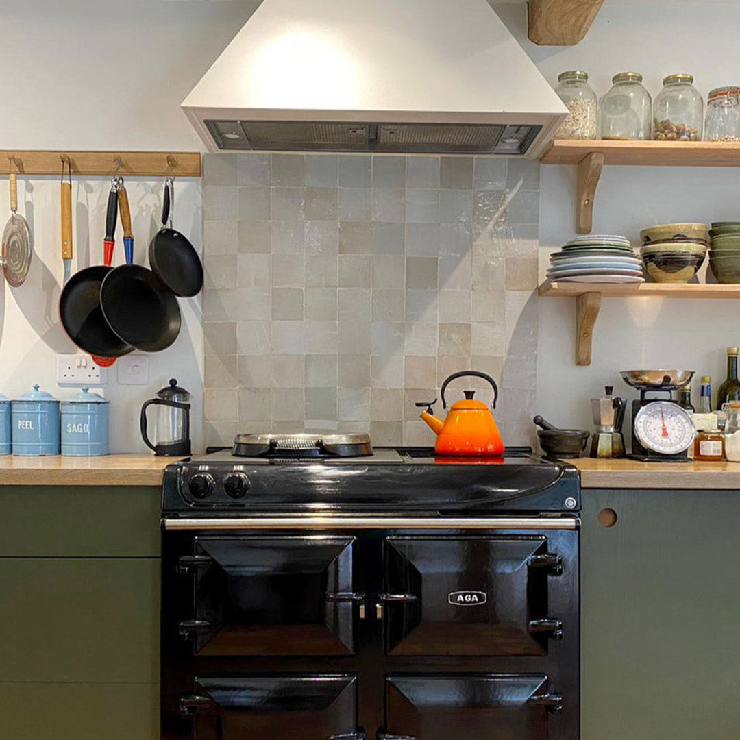 Black Aga range cooker in a kitchen with a tiled backsplash and wooden shelves.