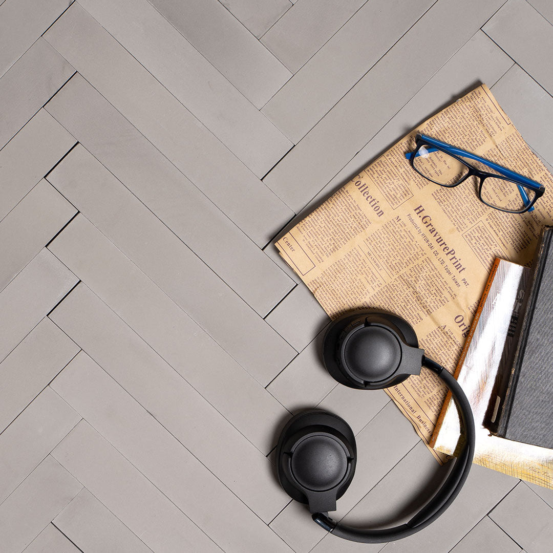 A rectangular herringbone pattern in light gray with a smooth matte finish, ideal for modern, minimalist, or industrial interior flooring and wall design applications.