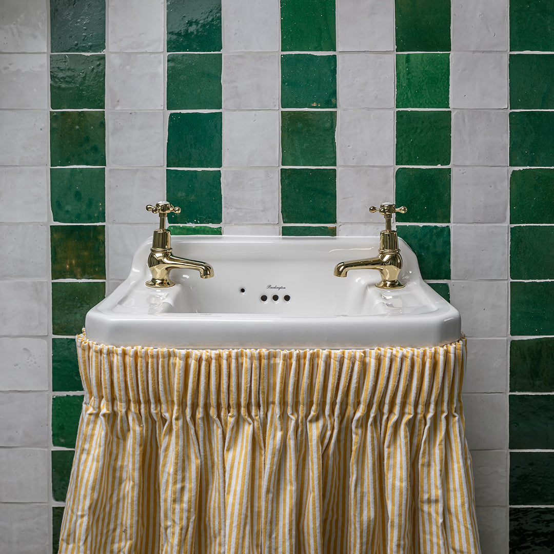 White sink with gold faucets against a green and gray tiled wall