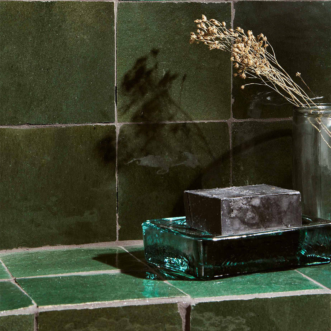 Green tiles with a glass container and soap on a counter