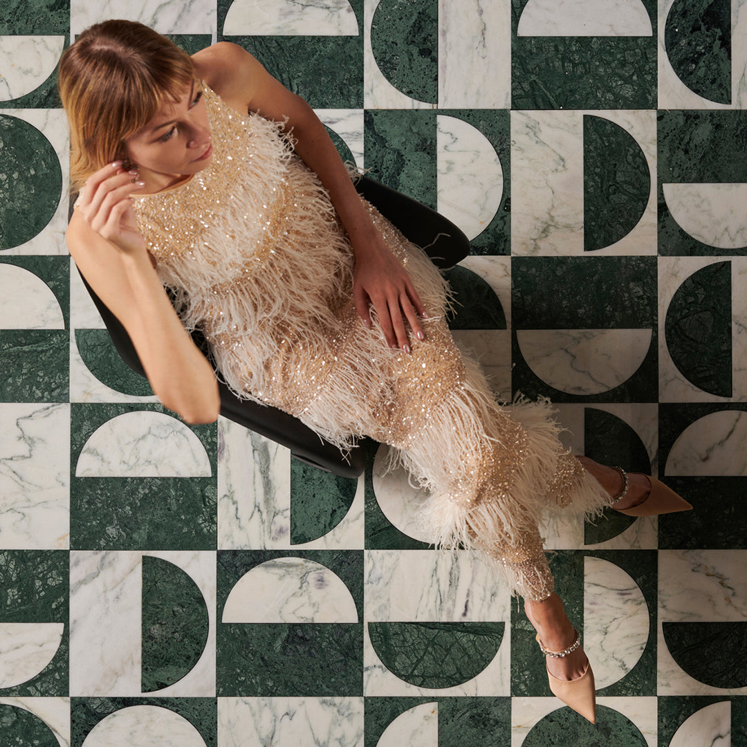 Woman in a sparkling dress sitting on a chair with a geometric marble-patterned floor.