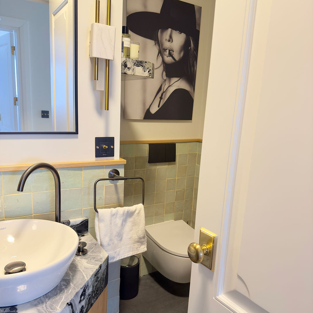 Contemporary bathroom with light green wall tiles, vessel sink, marble countertop, black fixtures, and bold artistic portrait