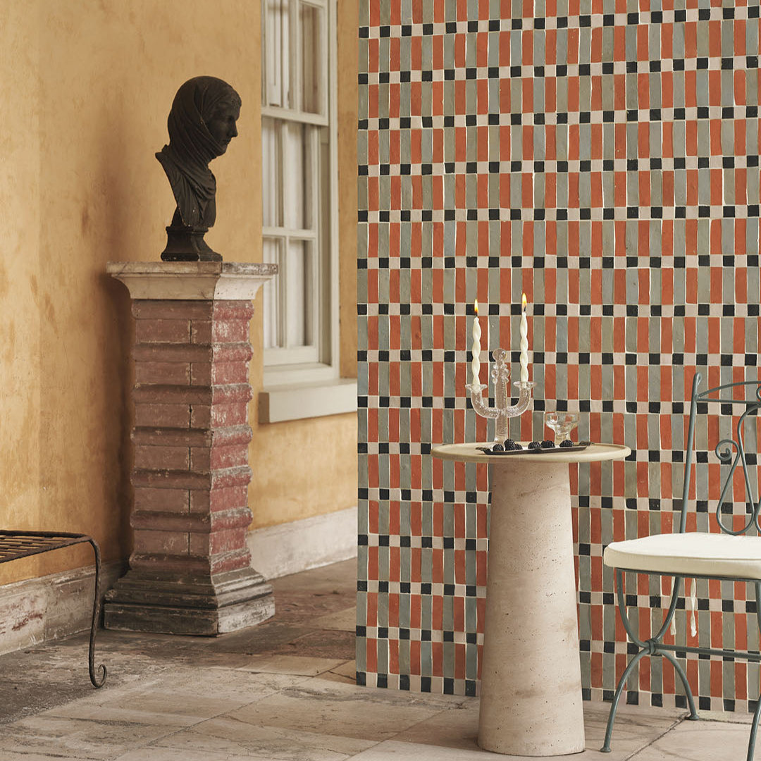 Decorative wall with geometric pattern, pedestal table, and bust sculpture in a room.