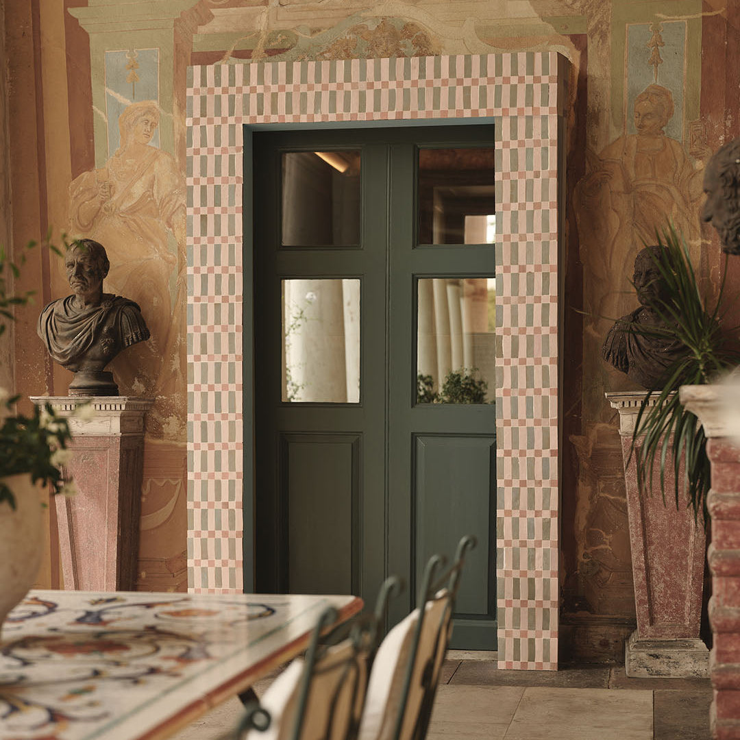 Decorative interior with a green door, classical statues, and patterned wall.