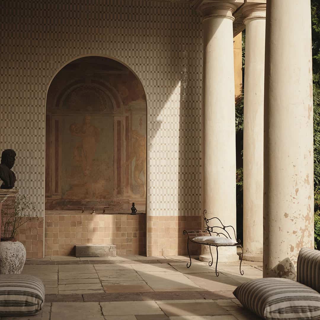  classical architectural setting with columns, wall frescoes, and a bench.