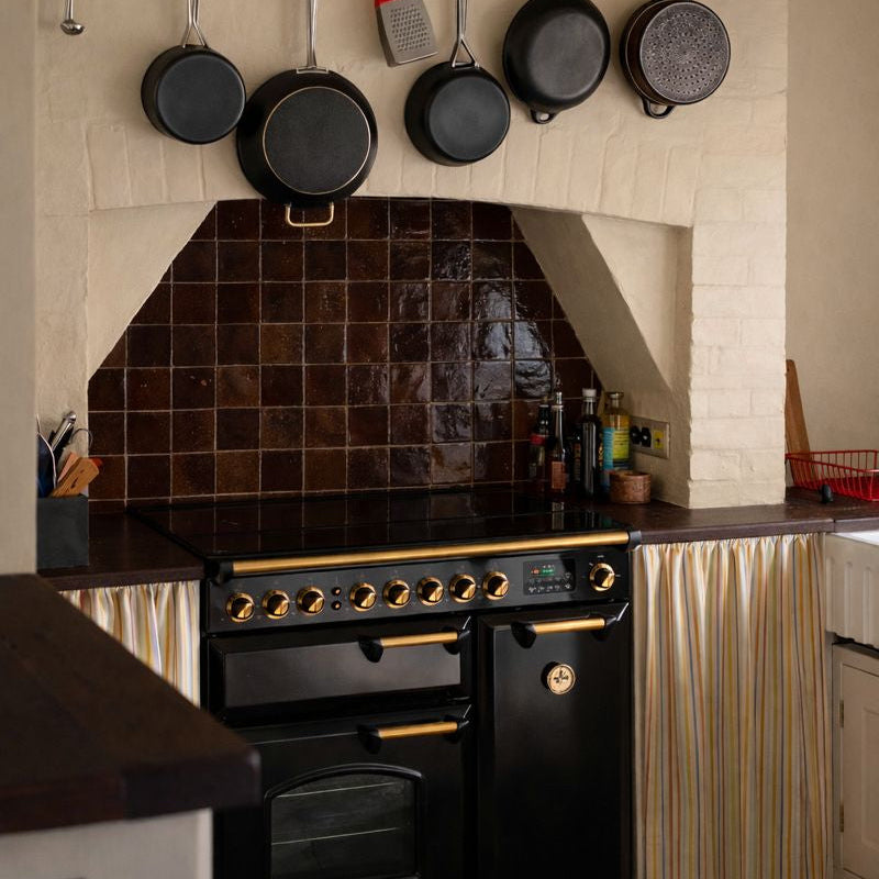 Modern kitchen with black appliances, hanging pans, and a tiled backsplash.