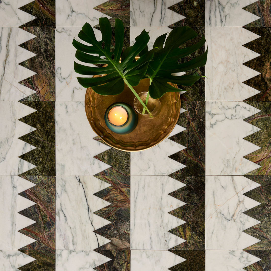 Decorative table setting with a gold bowl, candle, and leaves on a patterned marble surface.