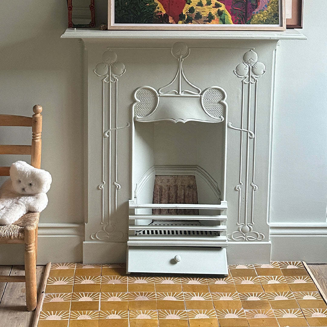 Decorative fireplace with intricate white surround, wooden chair with teddy bear, and patterned yellow floor.