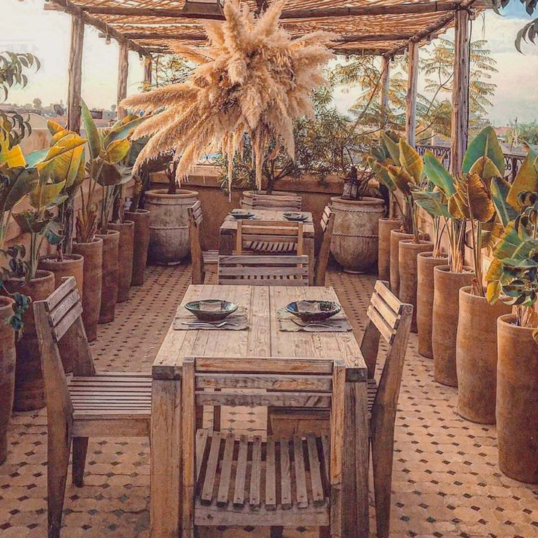 Outdoor dining area with wooden tables and chairs, potted plants, and a thatched roof.