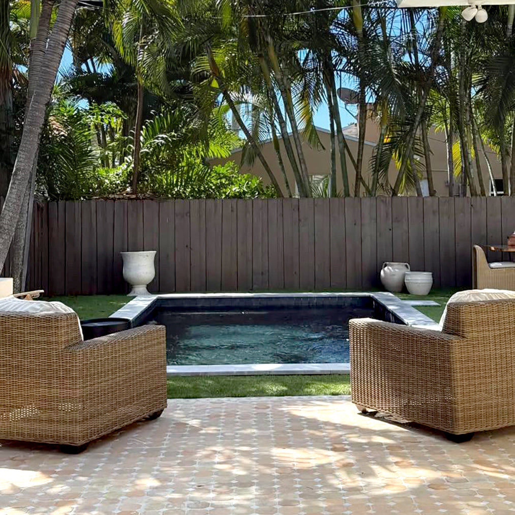 Outdoor patio with wicker chairs, a pool, and palm trees