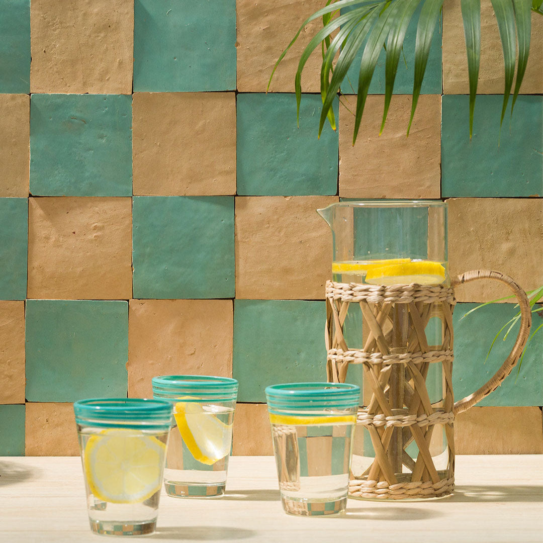 Glassware with lemon slices and a pitcher against a tiled wall.